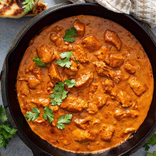 Chicken curry in a cast iron skillet, garnished with fresh cilantro, served with naan.