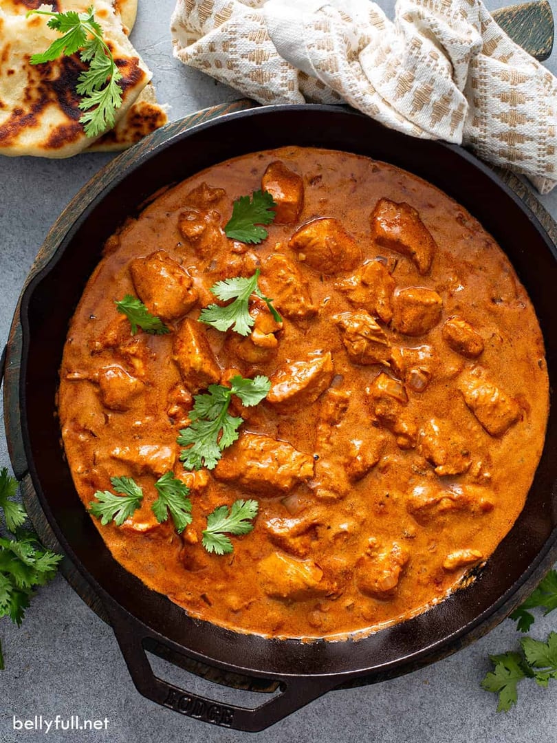 Chicken curry in a cast iron skillet, garnished with fresh cilantro, served with naan.