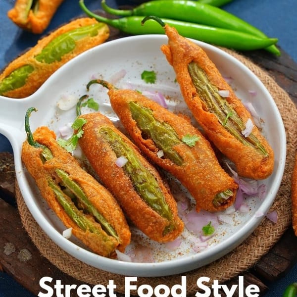 Deep-fried Mirchi Bajji on a white plate, garnished with chopped onions and cilantro, with whole chilies.