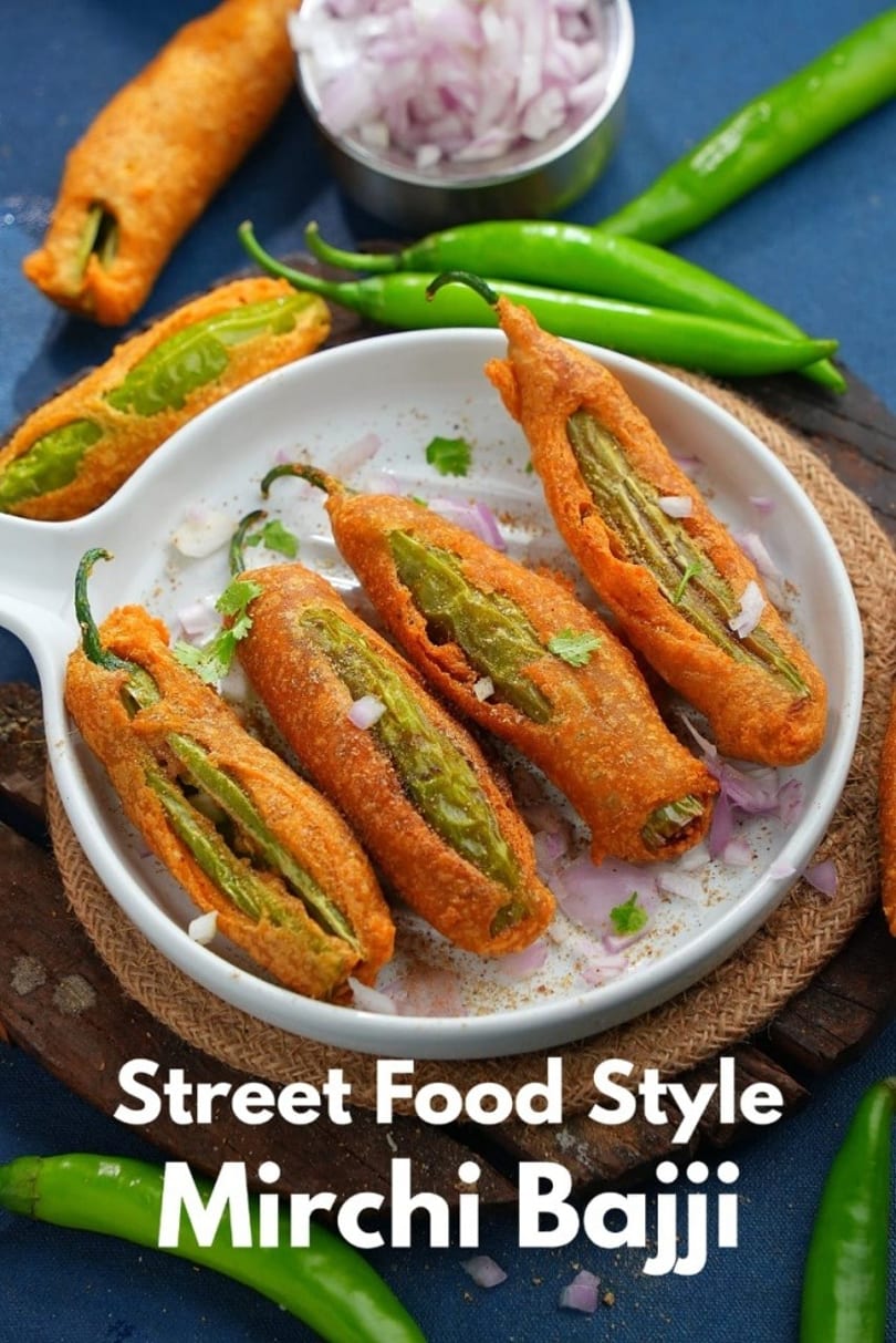 Deep-fried Mirchi Bajji on a white plate, garnished with chopped onions and cilantro, with whole chilies.