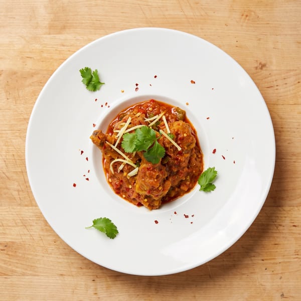 Chicken karahi, a Pakistani dish, garnished with cilantro and ginger on a white plate.