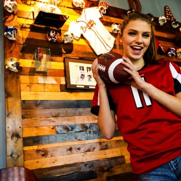 Smiling young woman in a red jersey holding a football in a sports-themed restaurant.