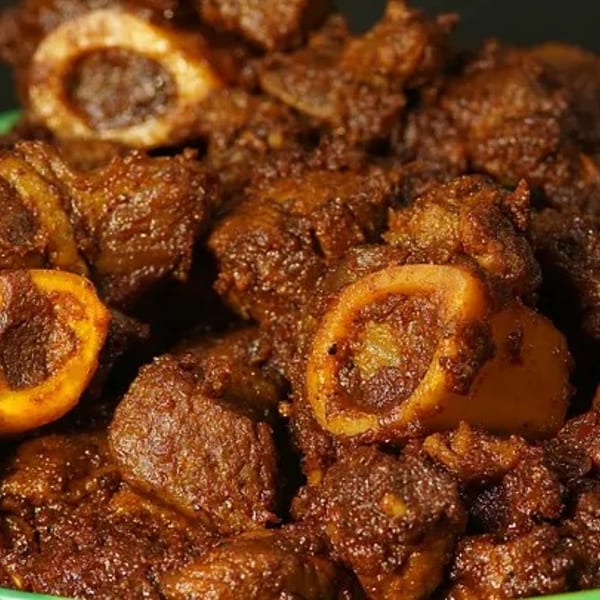 Close-up of dark brown, richly spiced meat pieces with bones in a green bowl.