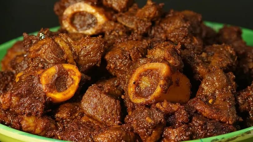 Close-up of dark brown, richly spiced meat pieces with bones in a green bowl.