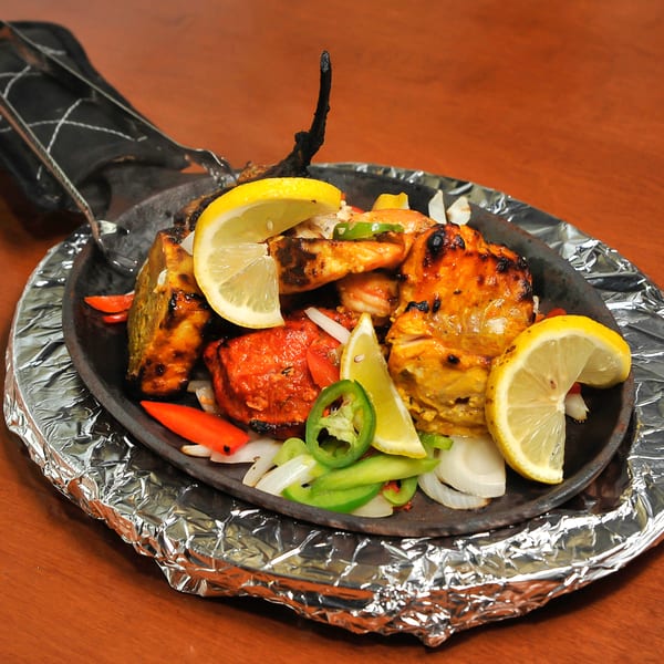 Mixed grill platter with chicken, shrimp, lemon, onions, and peppers on a sizzling cast iron pan.