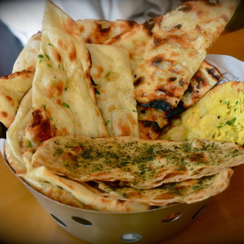 Assorted naan bread, including plain, herb, and charred varieties, served in a metal basket.