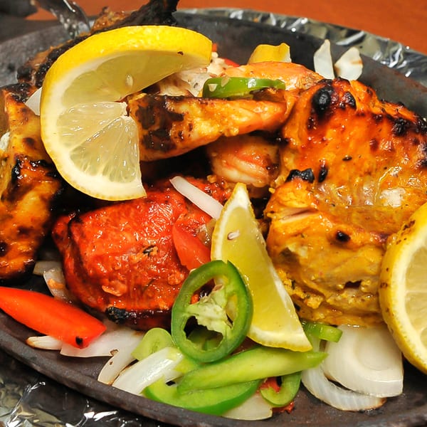 Sizzling platter of tandoori chicken, shrimp, and fish with fresh lemon and vegetables.