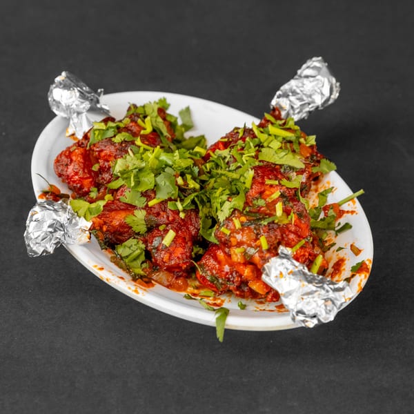 Red chicken lollipops with foil-wrapped bones, garnished with fresh cilantro on a white plate.