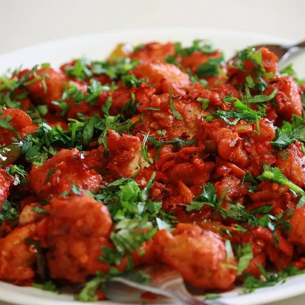 Vibrant red fried dish, generously garnished with fresh green cilantro, on a white plate.