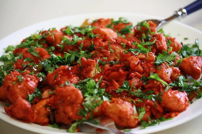 Vibrant red fried dish, generously garnished with fresh green cilantro, on a white plate.
