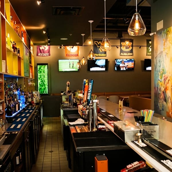 A vibrant bar interior with colorful shelves, multiple TVs, and a large mural on the wall.
