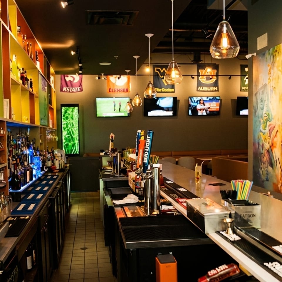 A vibrant bar interior with colorful shelves, multiple TVs, and a large mural on the wall.