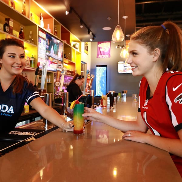 Bartender at ADDA Sport Pub serves a colorful drink to a customer in a Falcons jersey.