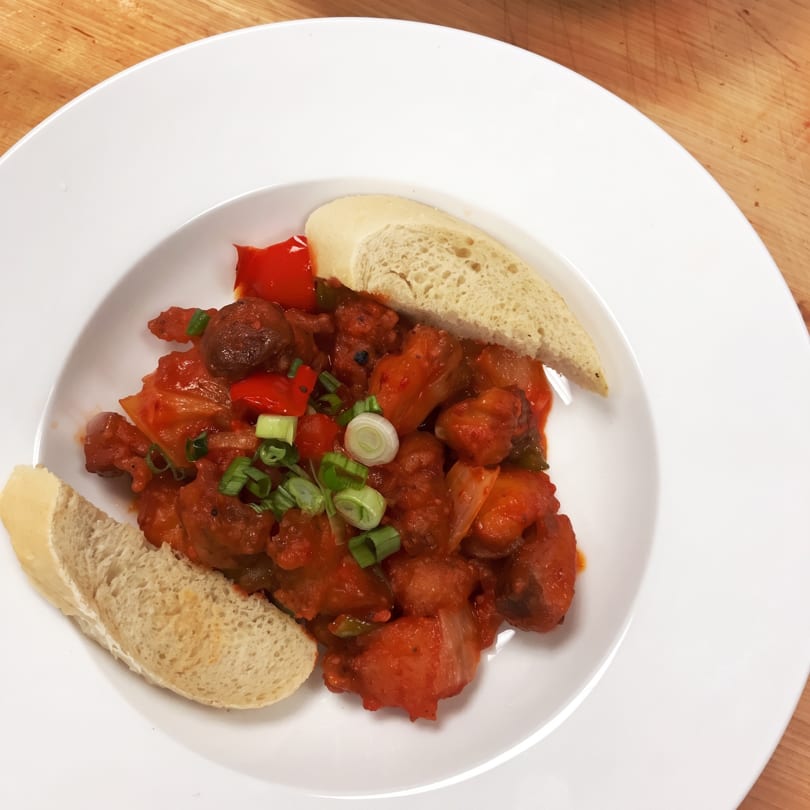Hearty stew with red sauce, peppers, and green onions, served with two slices of bread.