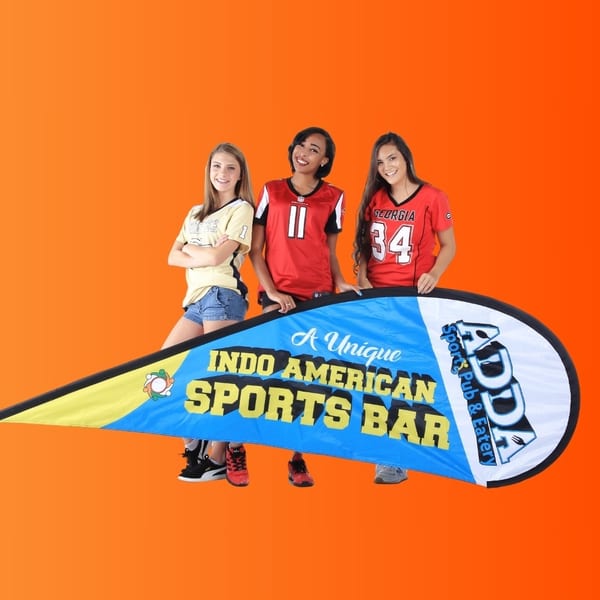 Three young women in sports jerseys posing behind an "Indo American Sports Bar" banner.