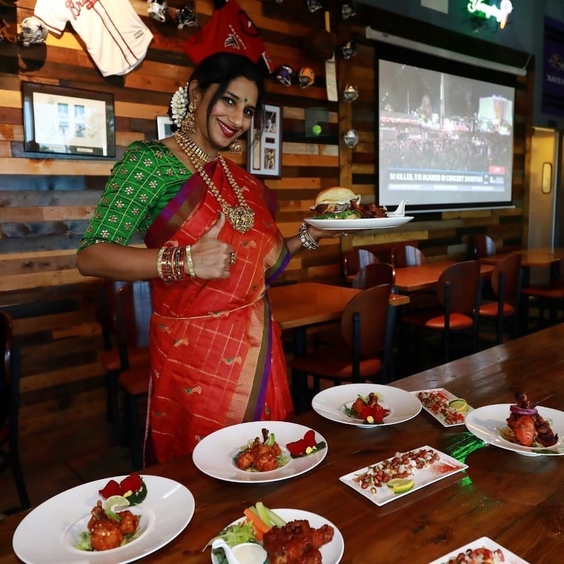 Woman in a red sari holding a burger and giving a thumbs up in a restaurant.