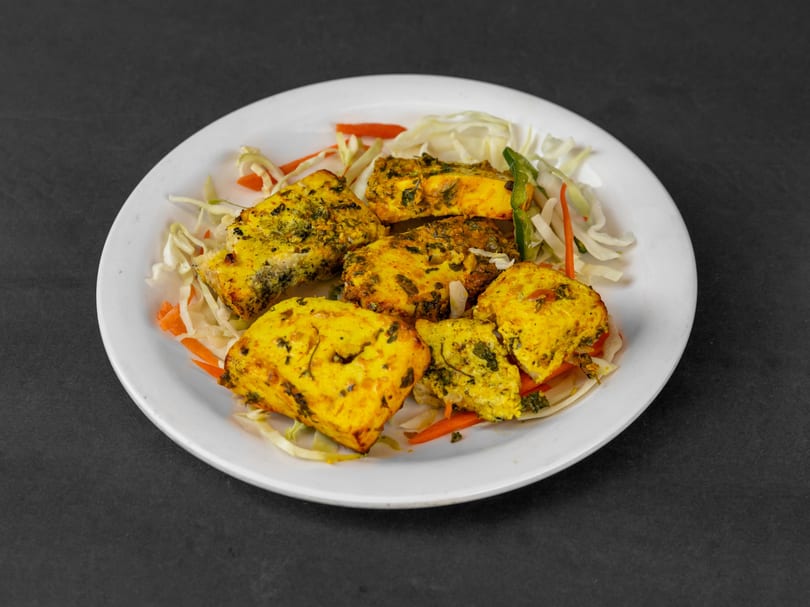 Yellow seasoned paneer pieces on a white plate with shredded cabbage and carrots.
